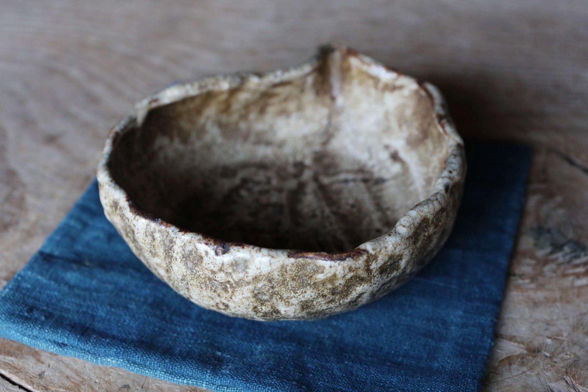 A ceramic bowl with a textured surface sits on a blue cloth on a wooden surface.