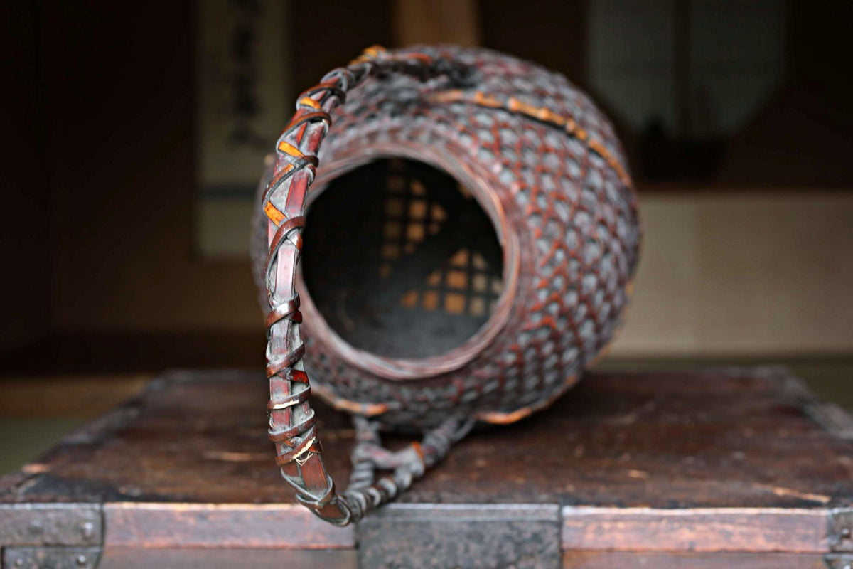 An old, weathered metal basket with a curved handle, sitting on a wooden surface.