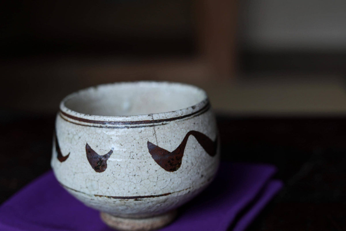 A white ceramic bowl with a decorative brown pattern on it, placed on a purple cloth.