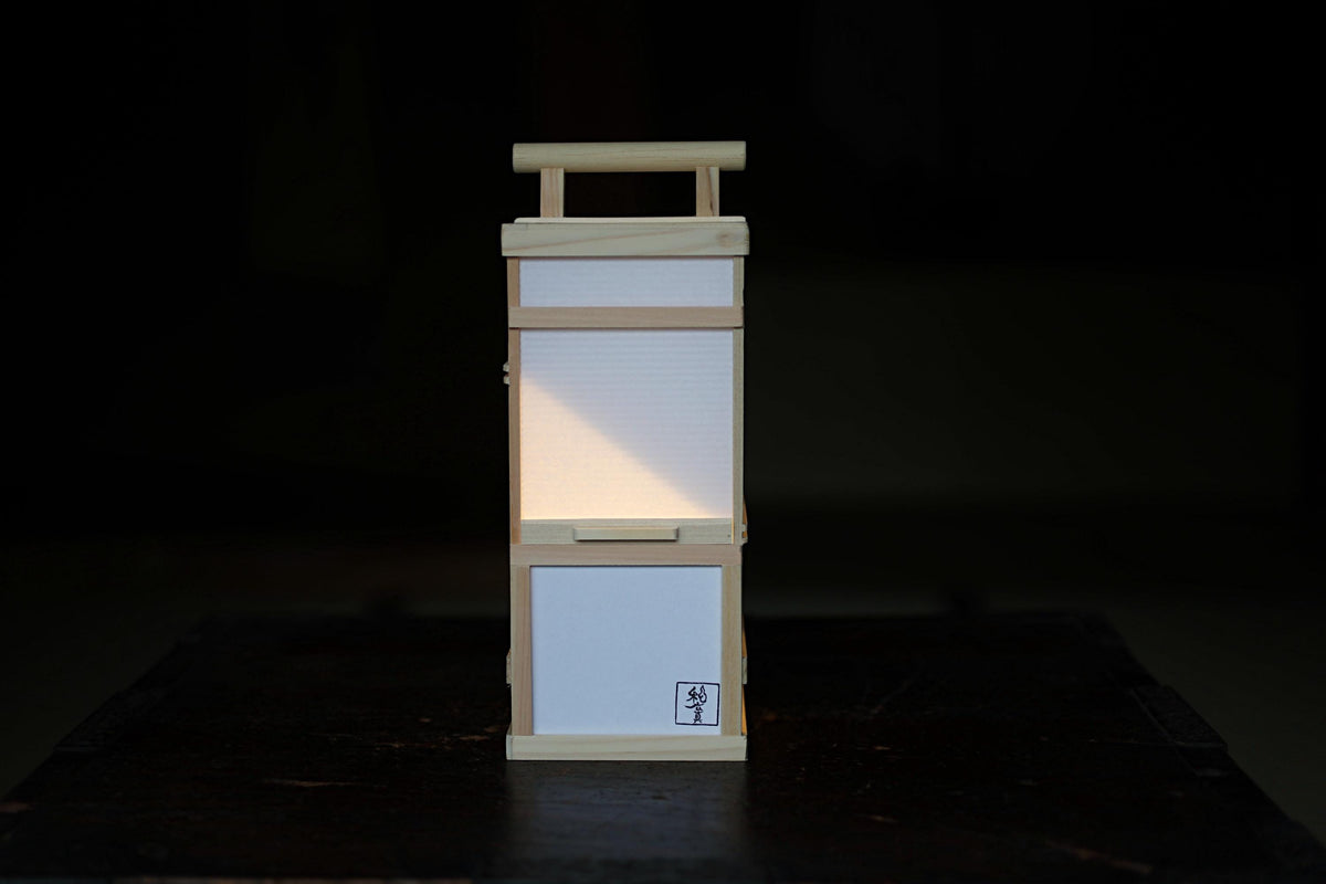 A small wooden lantern with a white paper panel on the front, placed on a dark surface.