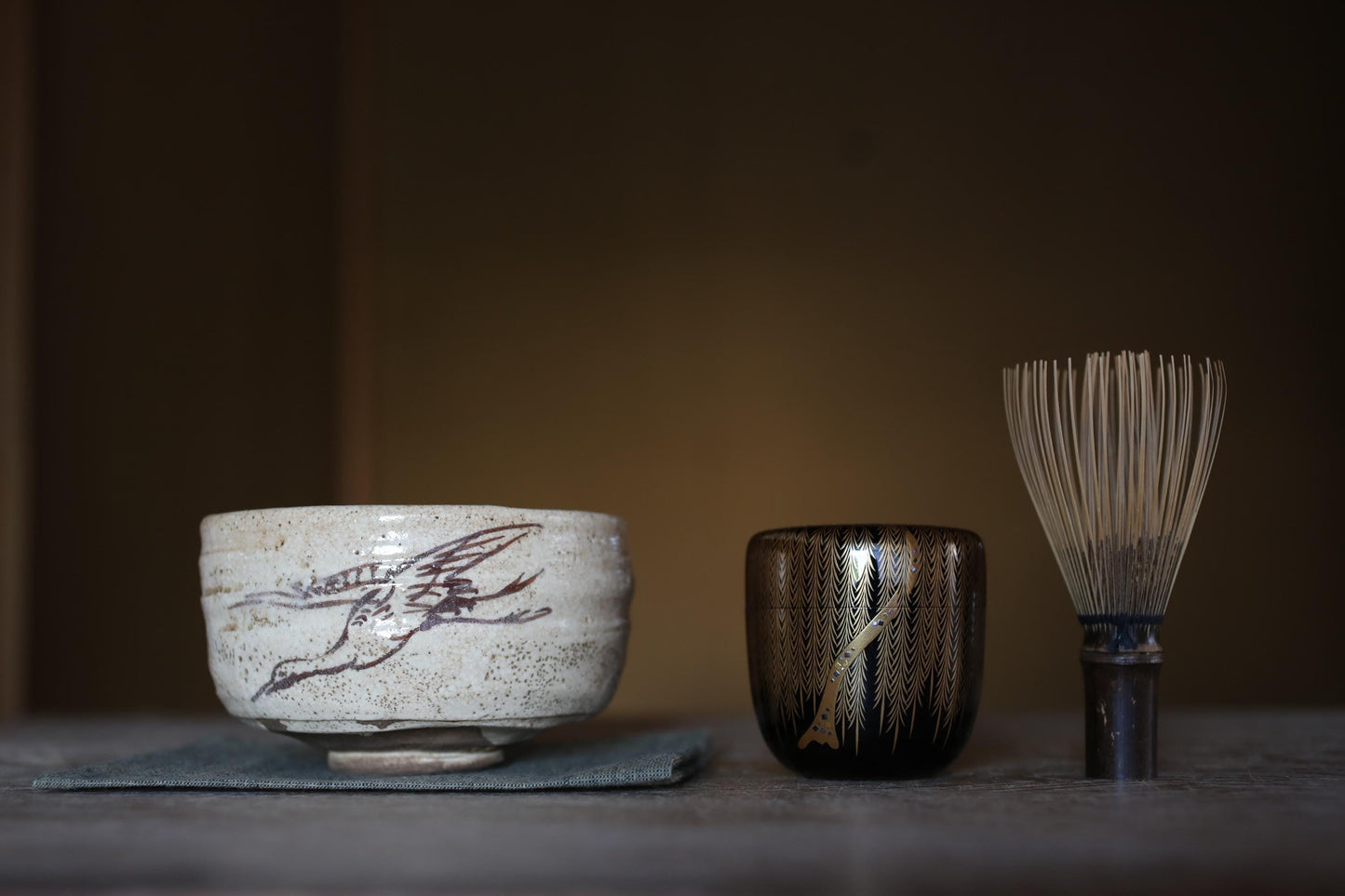 a ceramic bowl with a bird design, a small black container, and a whisk on a table.
