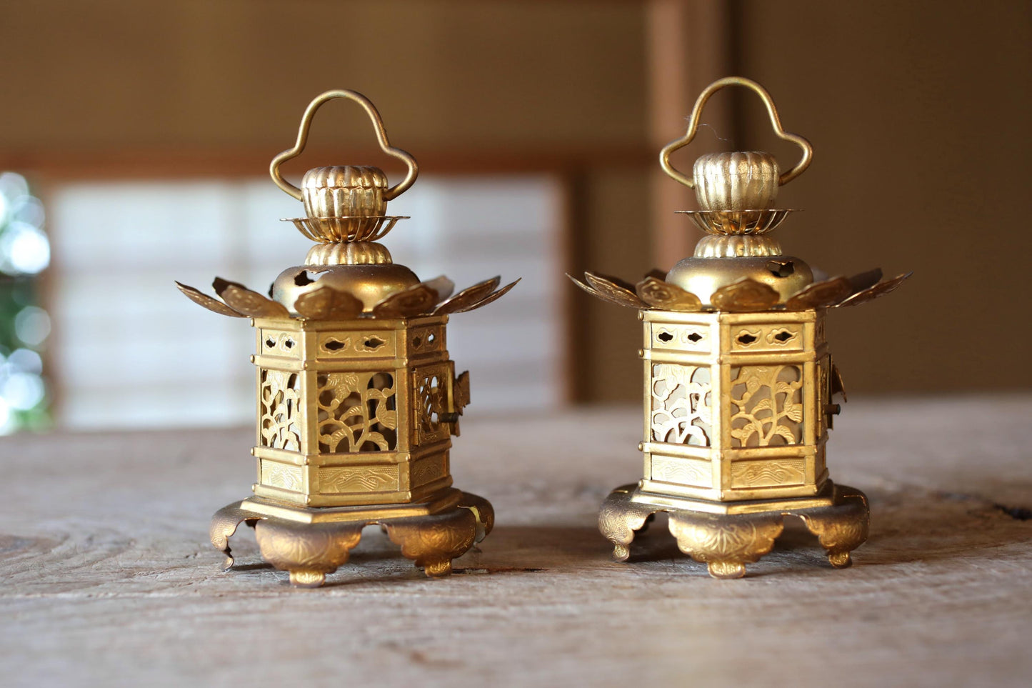 Two ornate brass lanterns with intricate designs, placed side by side on a wooden surface.