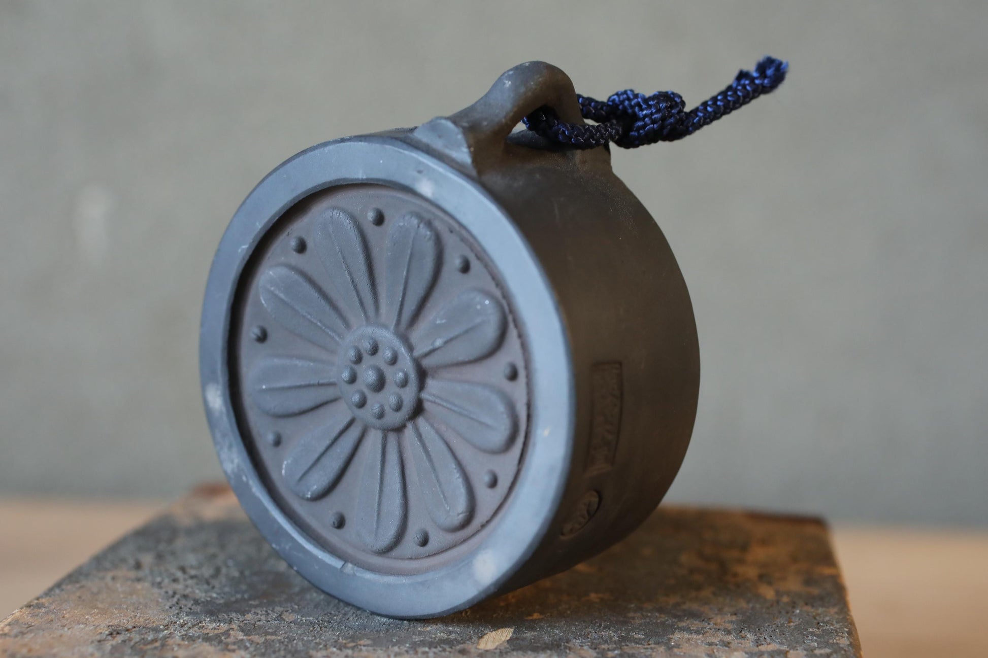 A gray ceramic object with a flower-like design on it, hanging from a string.