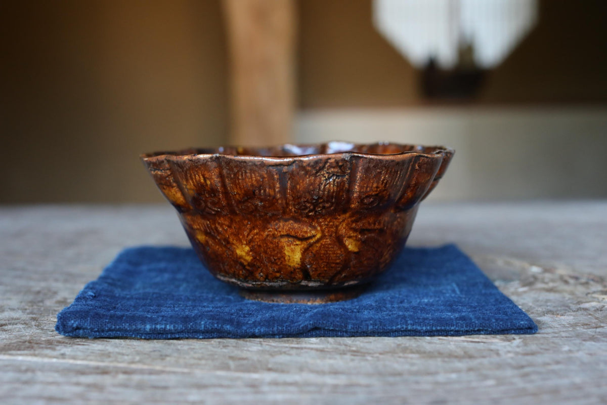 A brown ceramic bowl with a scalloped edge sits on a blue cloth on a wooden surface.