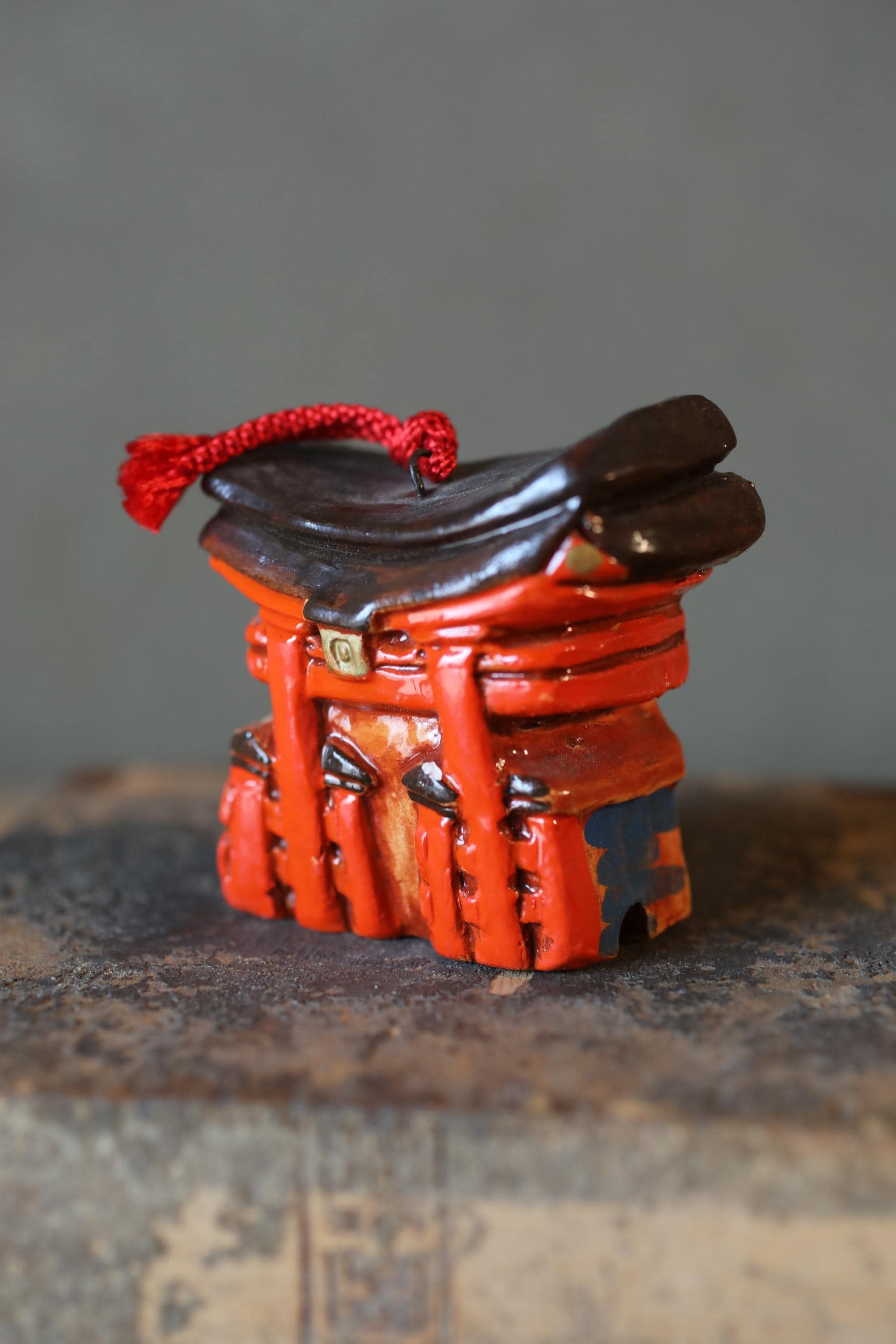 A close-up image of a small, red and black object with a tassel attached, mounted on a metal surface.