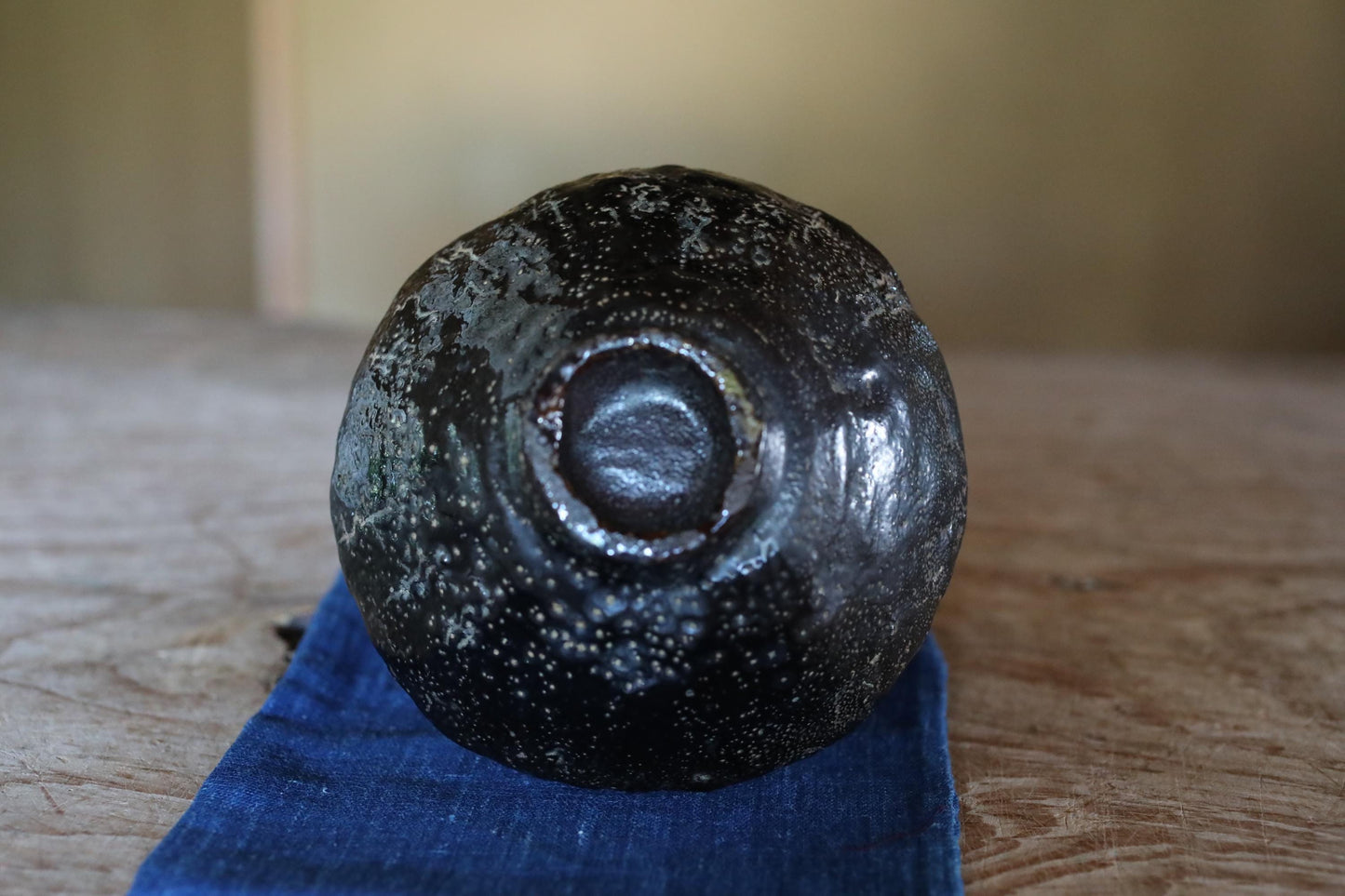 A black, speckled object with a circular opening is sitting on a blue cloth on a wooden surface.