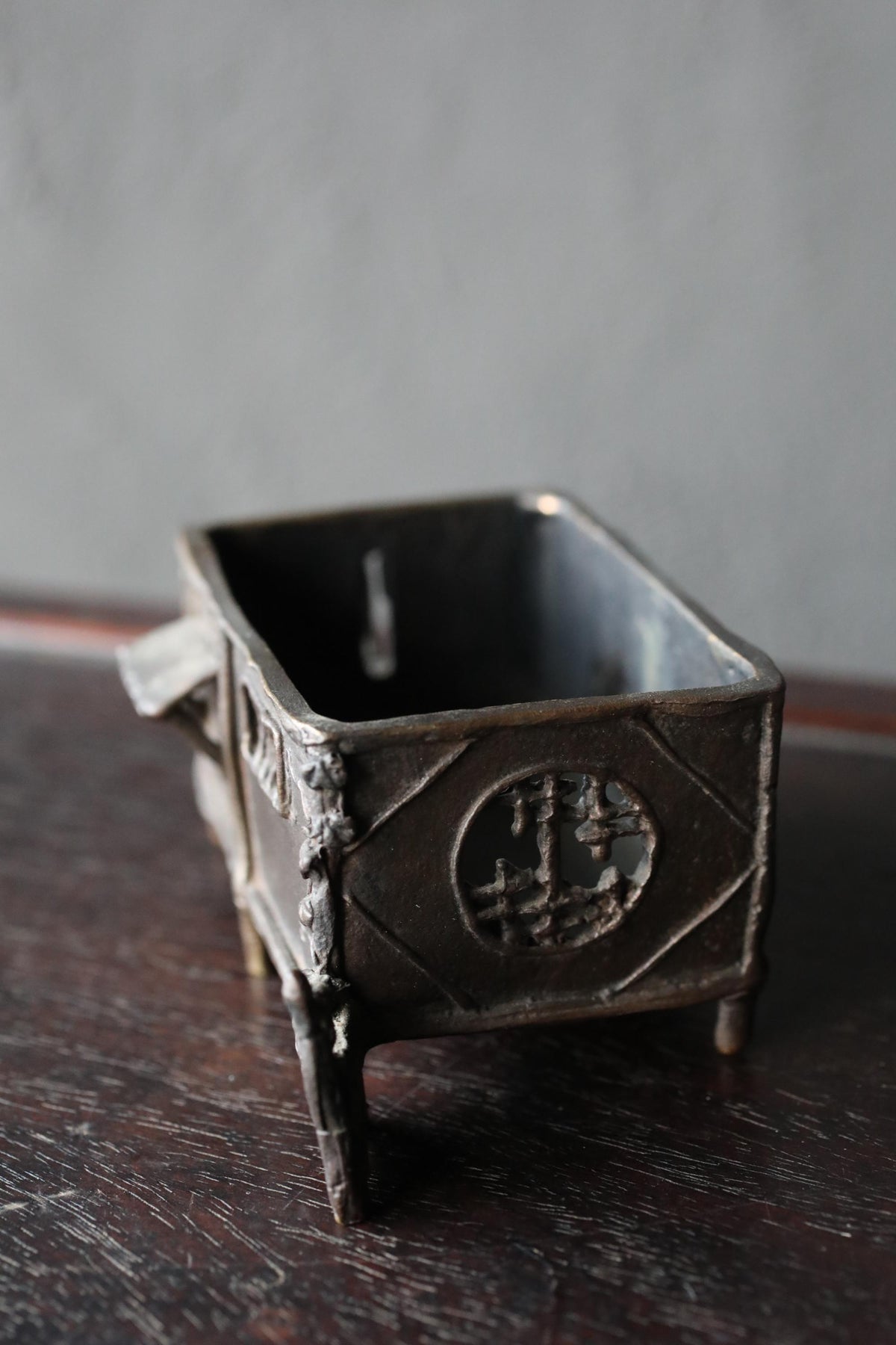A small, rectangular metal container with a decorative design on the front, sitting on a wooden surface.