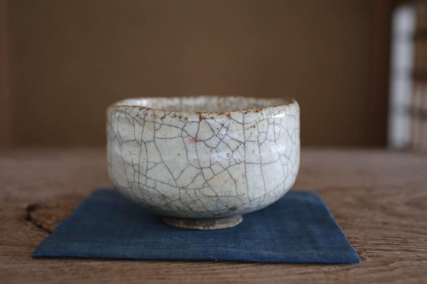 A white ceramic bowl with a cracked and textured surface sits on a blue cloth on a wooden table.
