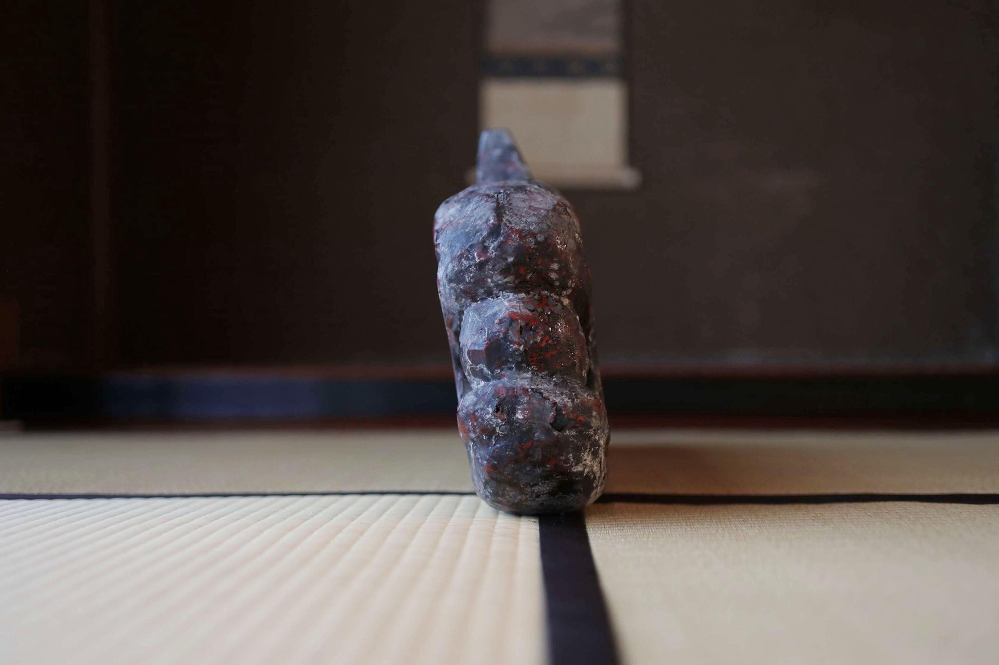 A dark, textured object resembling a piece of metal or stone is positioned on a white surface, with a black line running across it.