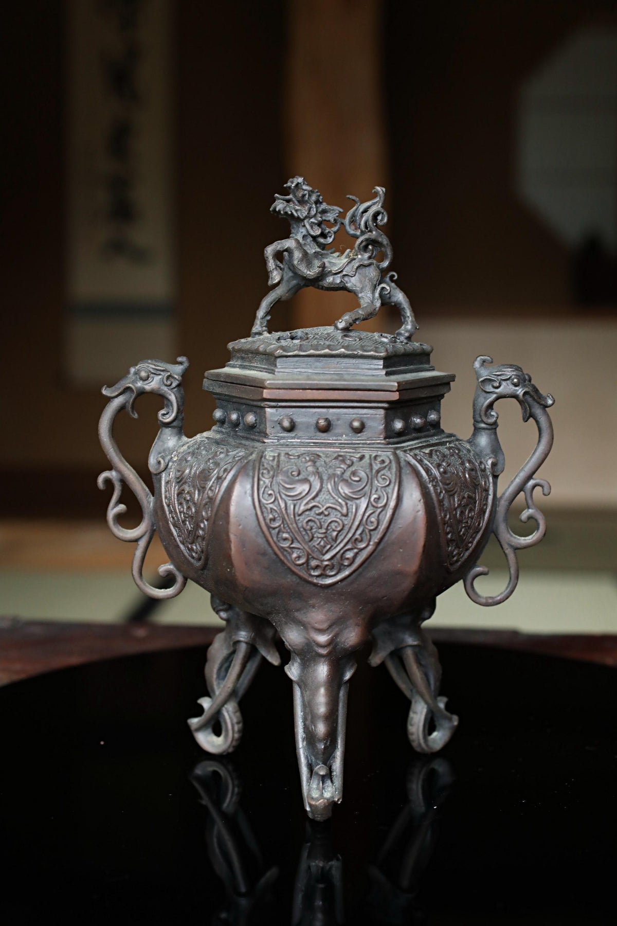 An ornate bronze incense burner with intricate designs and a dragon figure on top, placed on a black surface.