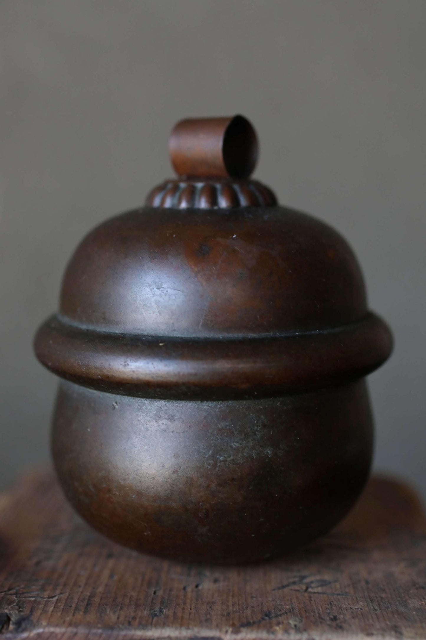 A dark brown, round metal container with a small, round top sits on a wooden surface.