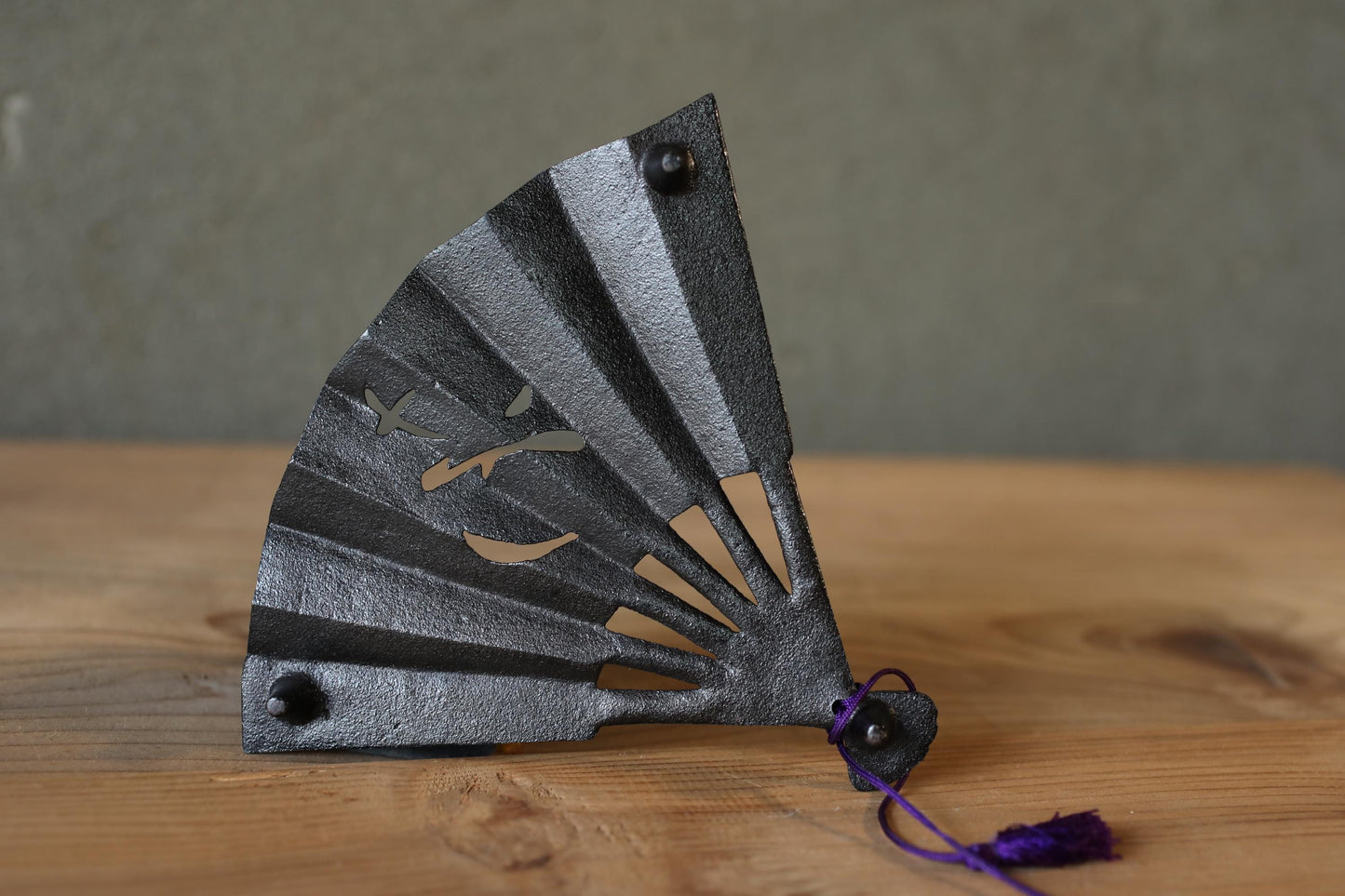 A black metal fan with a purple tassel is placed on a wooden surface.