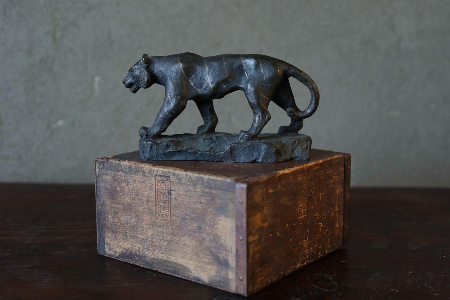 A bronze sculpture of a panther is displayed on a wooden crate, which is placed on a wooden surface.