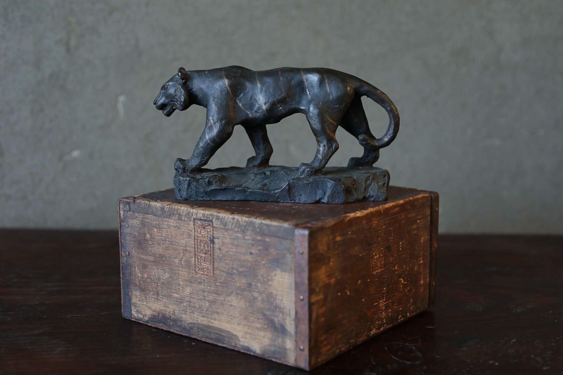 A bronze sculpture of a panther is displayed on a wooden crate, which is placed on a wooden surface.