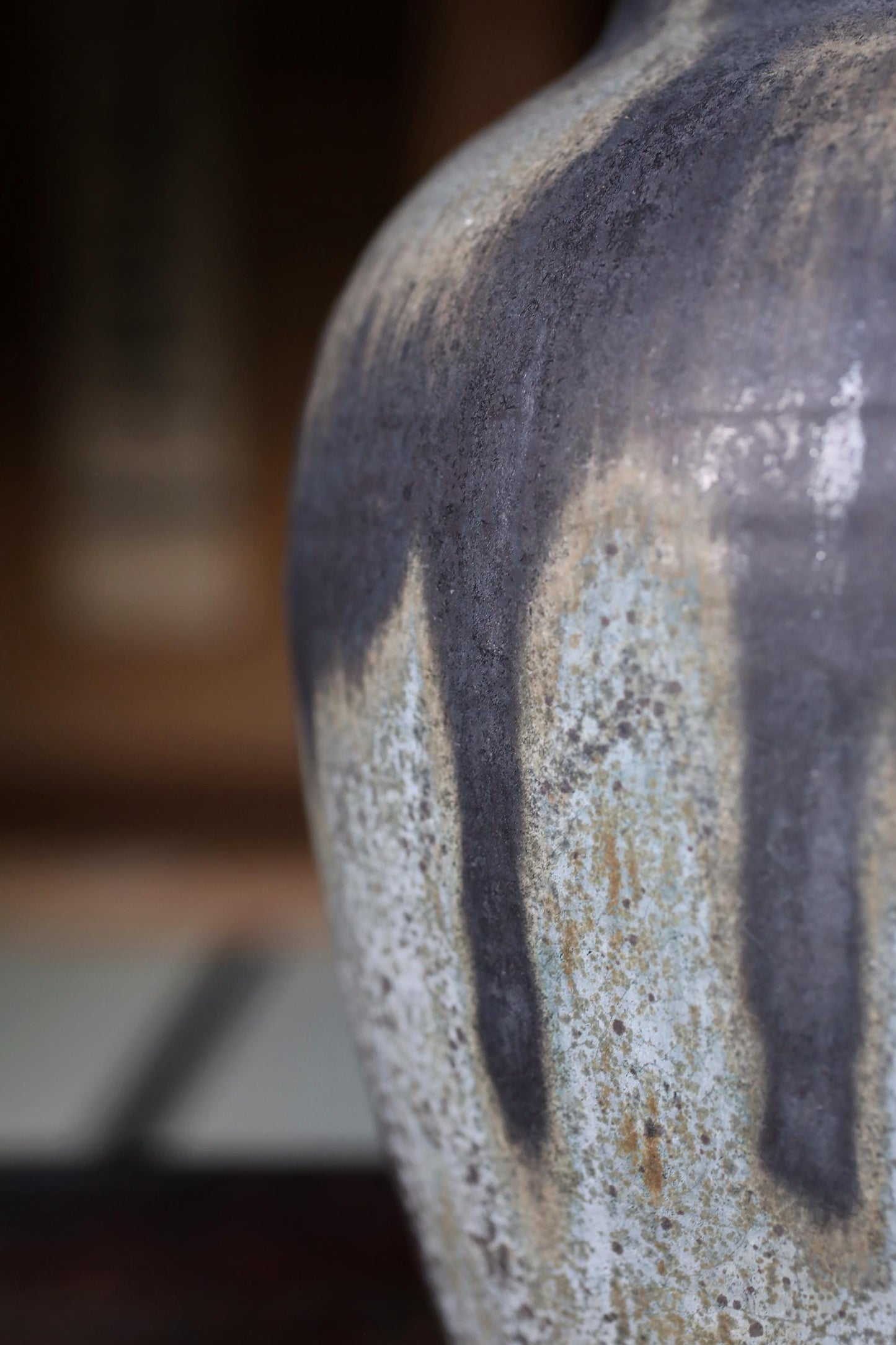 A close-up view of a textured ceramic vase with a dark gray and white color scheme, featuring a pattern of vertical lines and speckles.