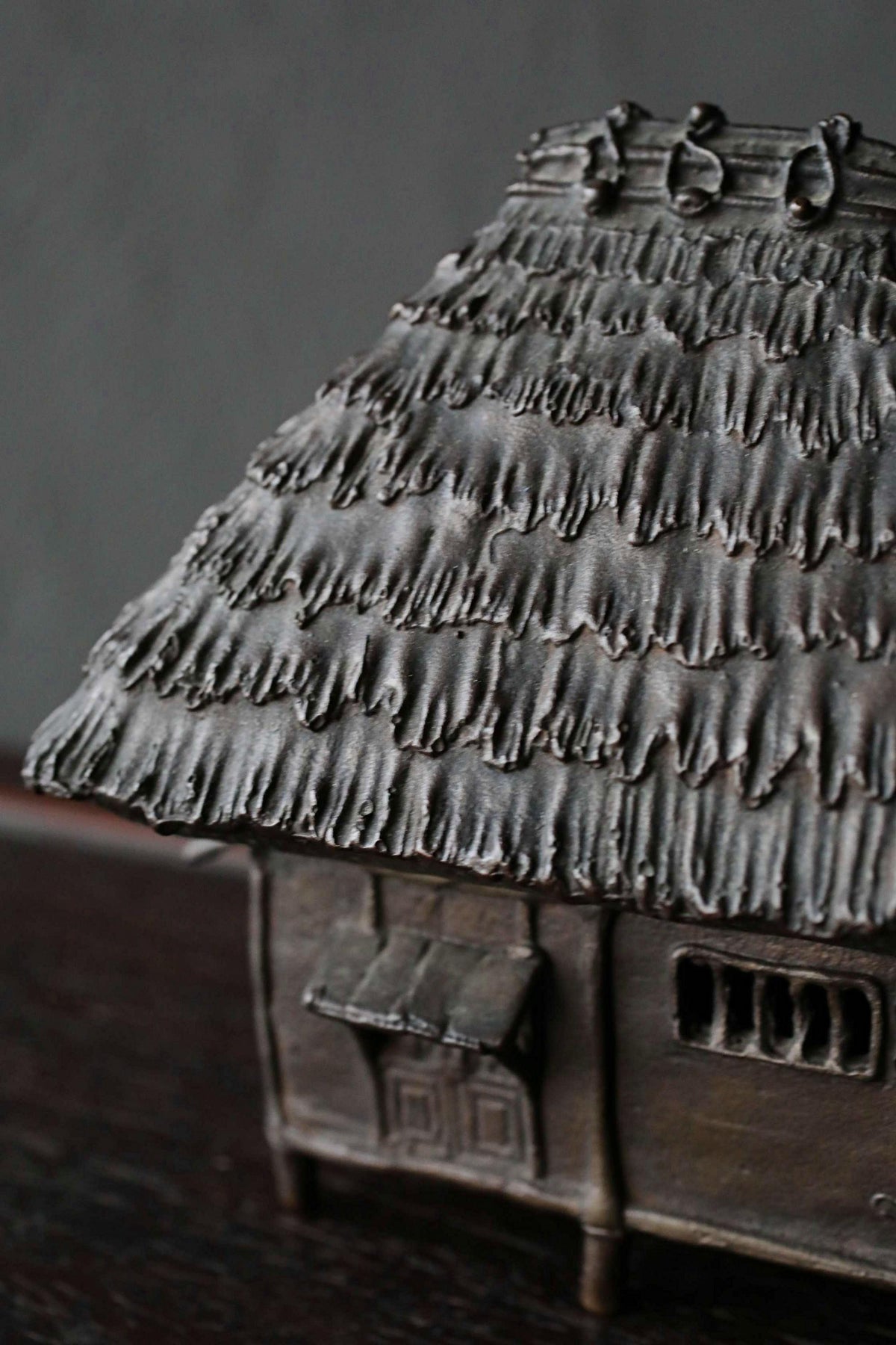 A close-up view of a small, intricately designed metal house with a thatched roof, sitting on a dark surface.