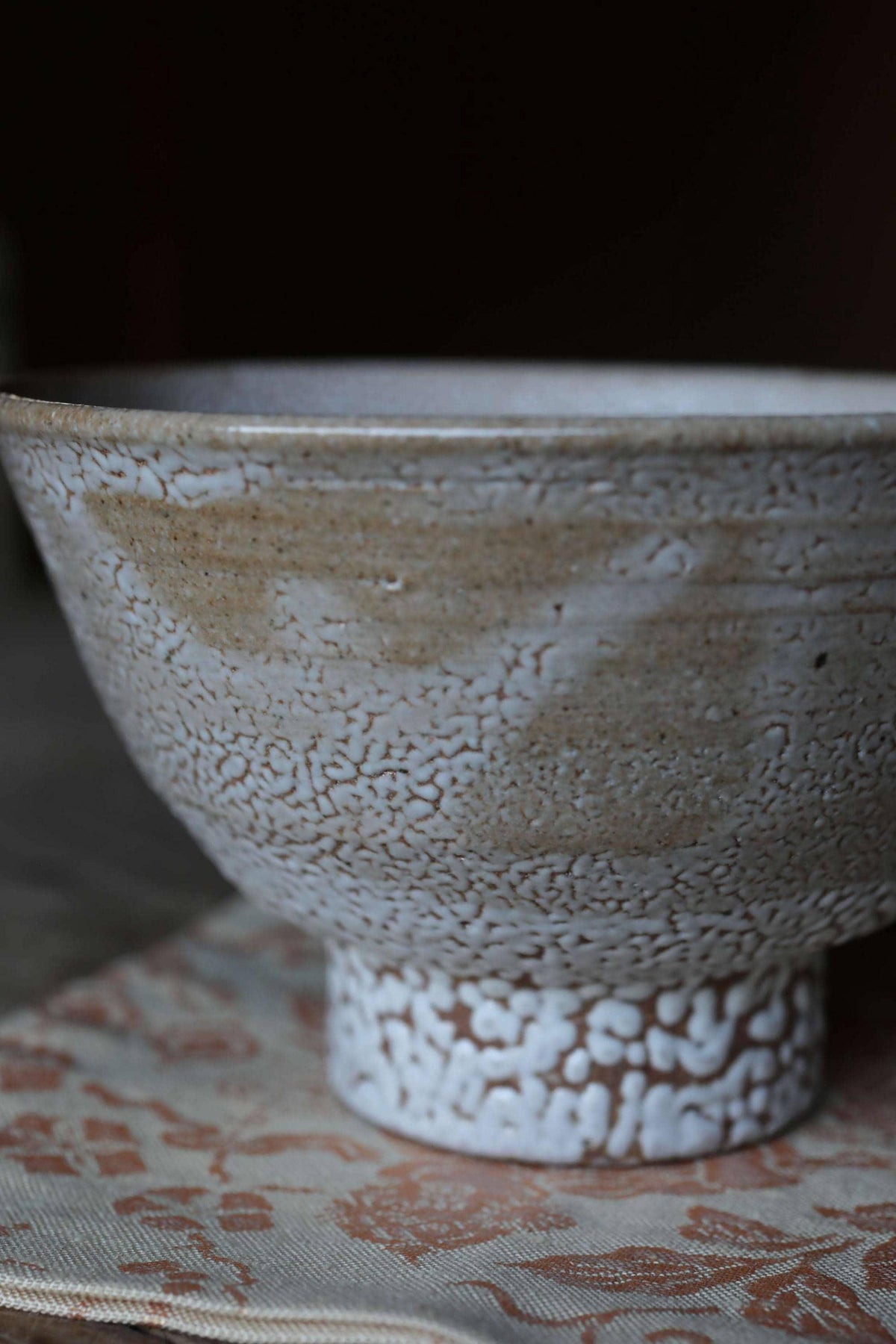 A close-up image of a white ceramic bowl with a textured surface, resting on a patterned fabric.