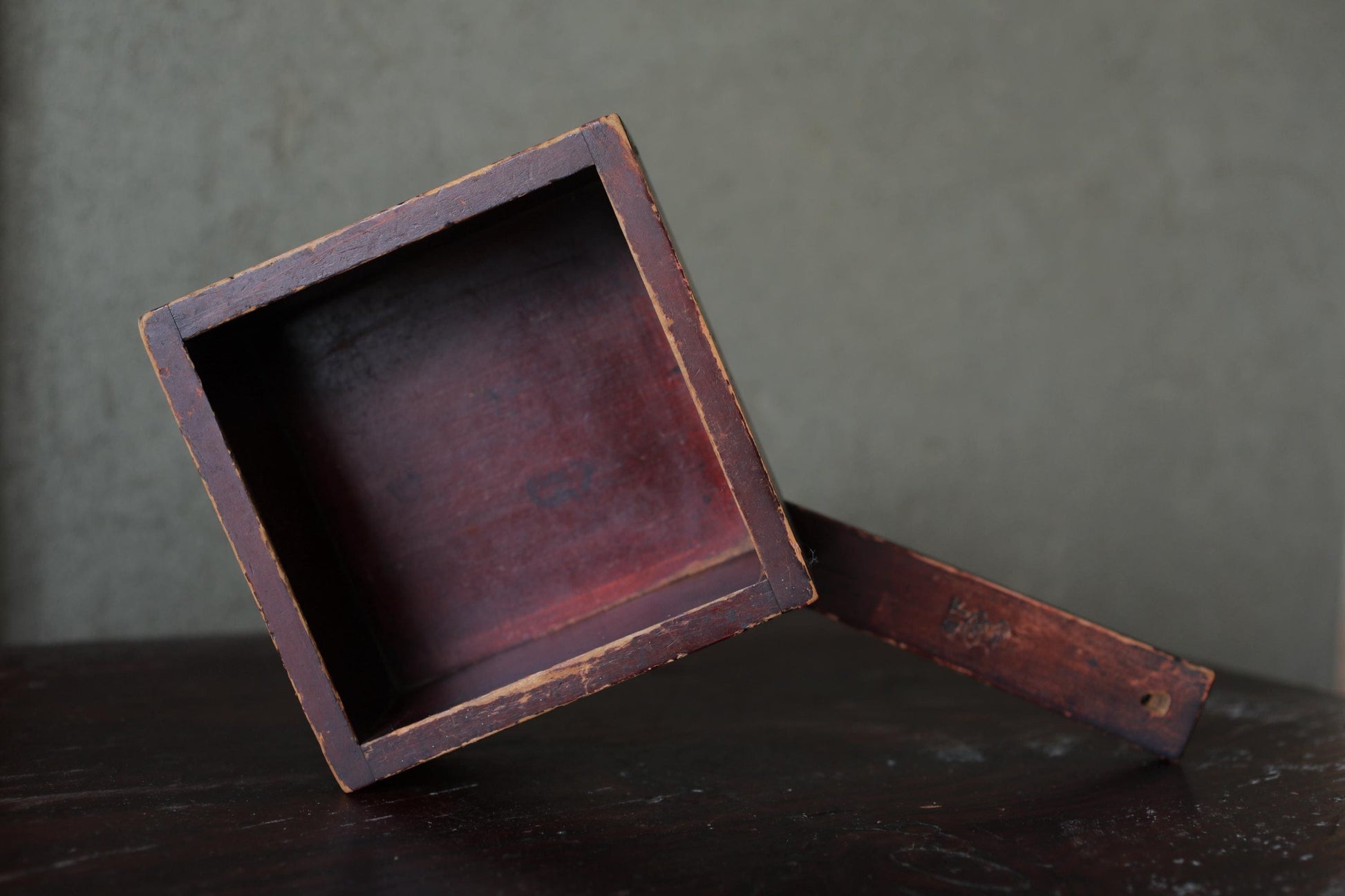 An old, weathered wooden box with a visible interior, sitting on a dark surface against a gray background.