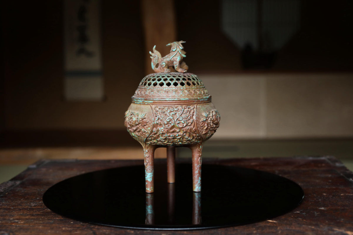 An ornate bronze incense burner with a dragon design on top, placed on a black circular tray.