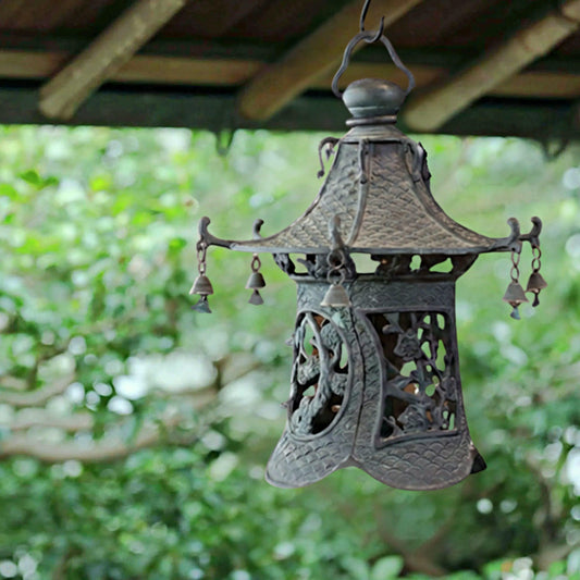 An ornate, antique-style lantern with intricate metalwork and hanging bells, suspended from a wooden structure.