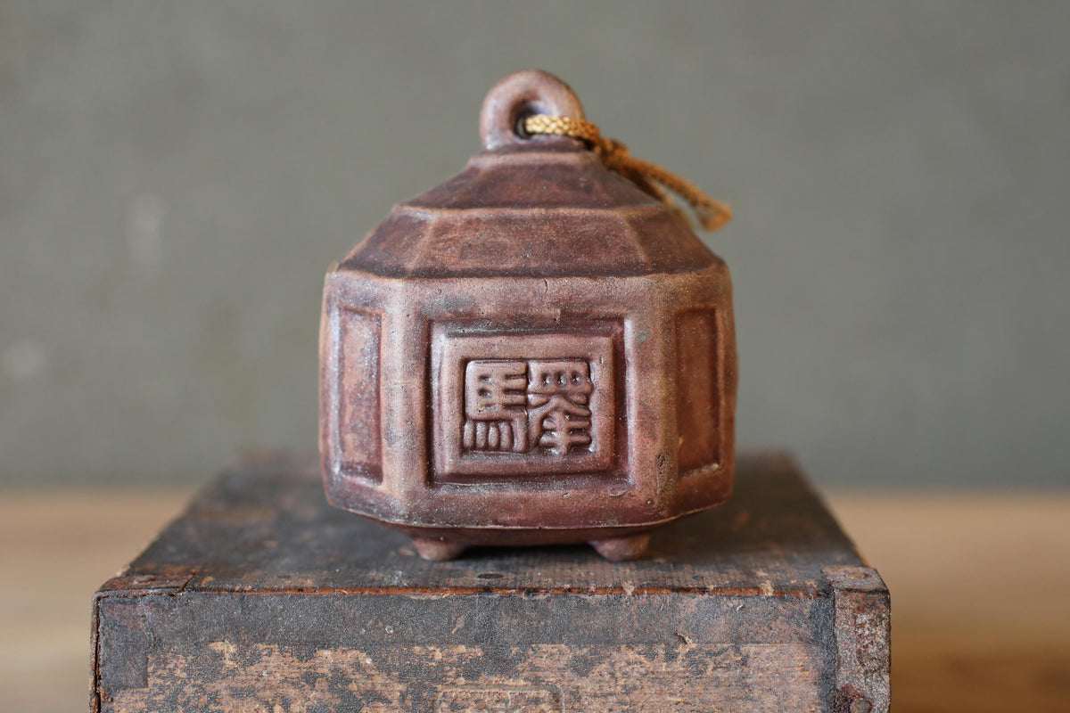 A brown ceramic bell with a decorative design on it, sitting on a wooden surface.