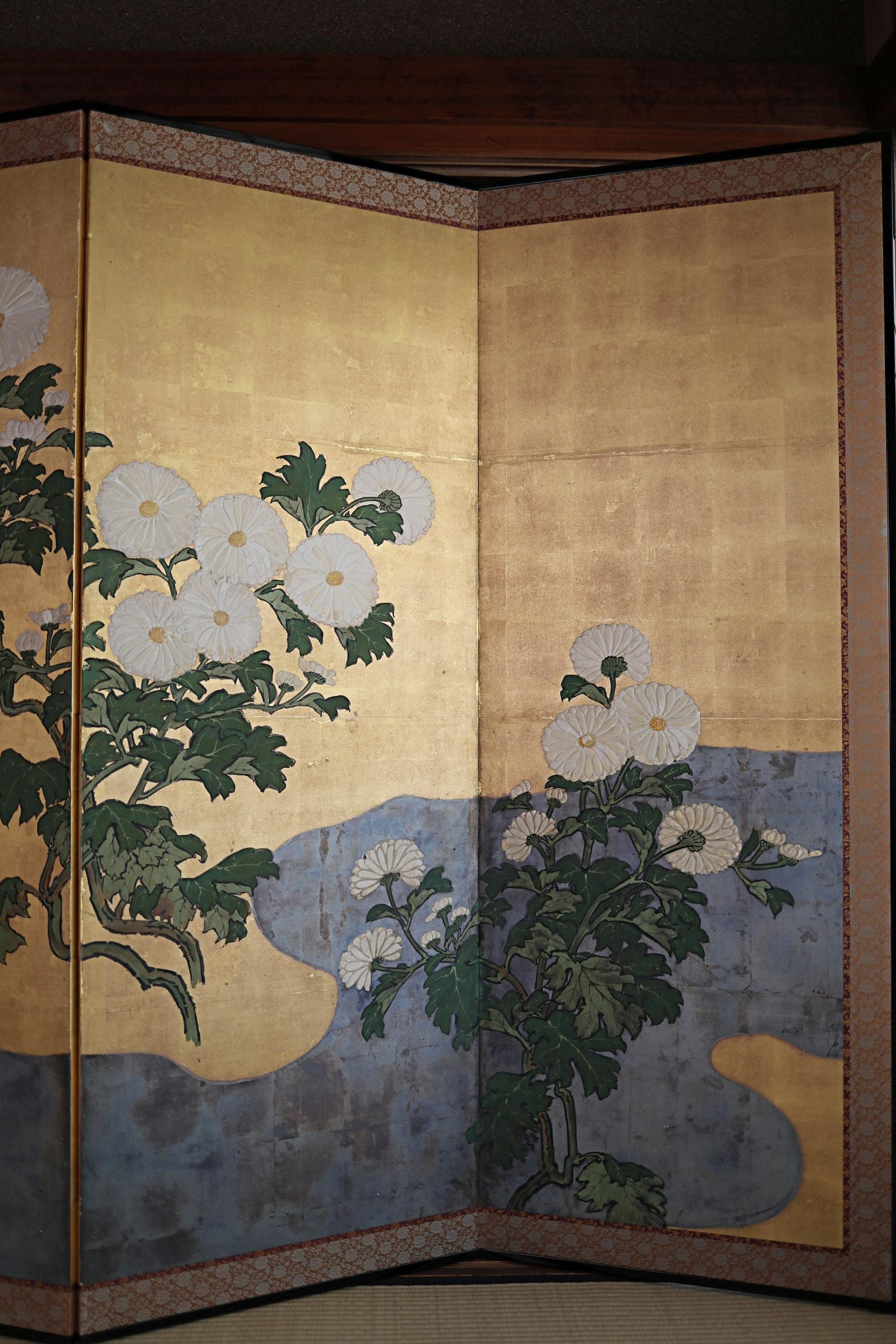 a large, intricately designed screen with a floral motif. The screen is divided into two sections, with the left side showcasing white flowers and green leaves, and the right side featuring white flowers and green leaves. The overall design is visually appealing and detailed, with the flowers and leaves adding a sense of nature and beauty to the composition.
