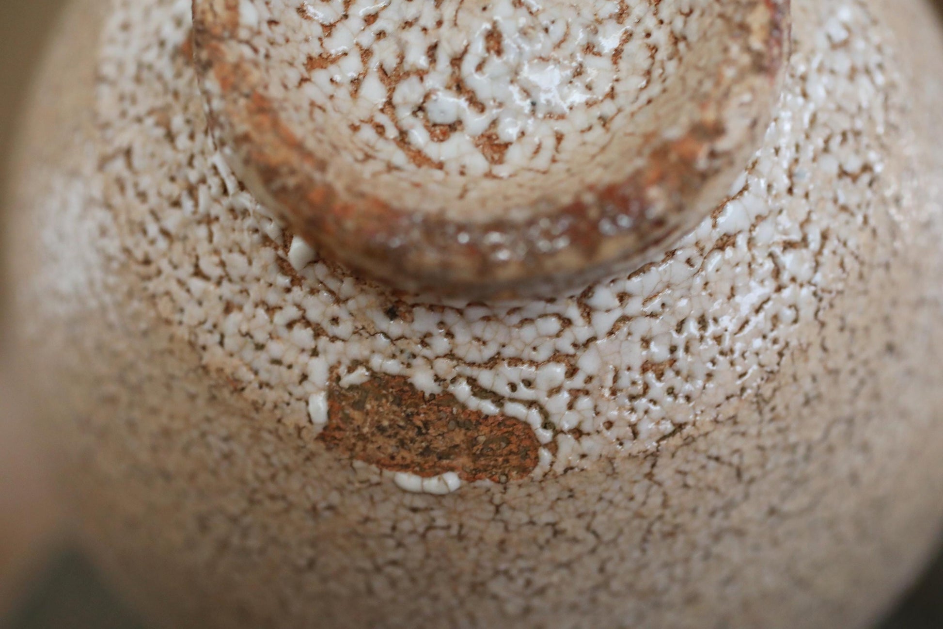 A close-up view of a textured ceramic object, possibly a vase or bowl, with a speckled, speckled pattern and a small, irregularly shaped hole or crack in the center.