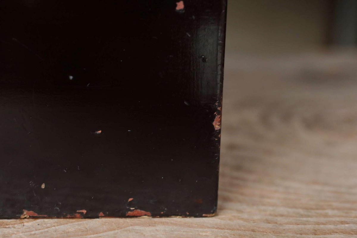A close-up view of a dark, textured surface, possibly a piece of furniture or a wall, with a slightly worn and weathered appearance.