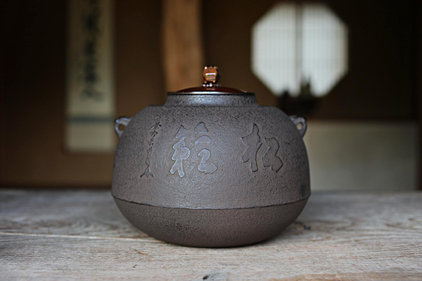 A black ceramic teapot with Chinese characters on it, placed on a wooden surface.