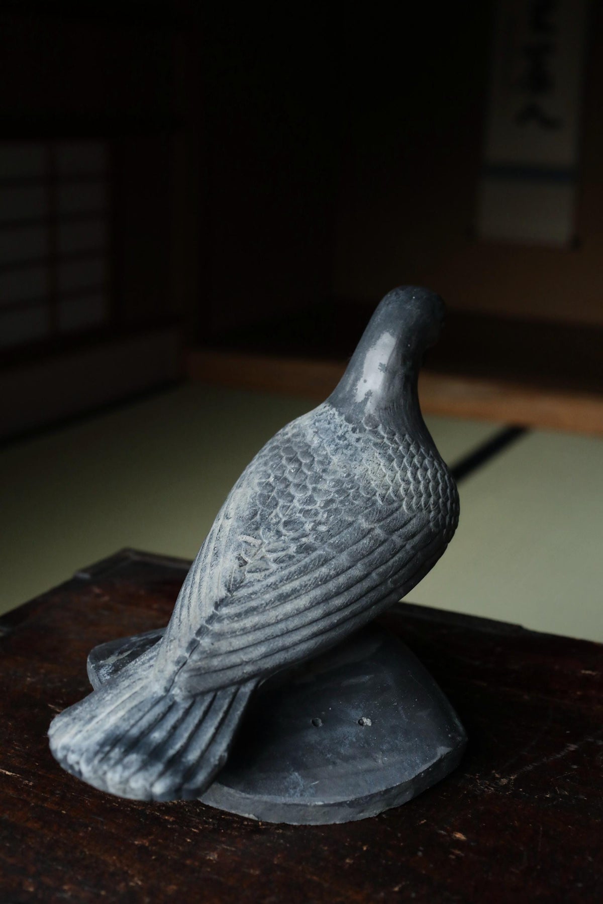 A gray stone bird figurine is perched on a wooden surface.