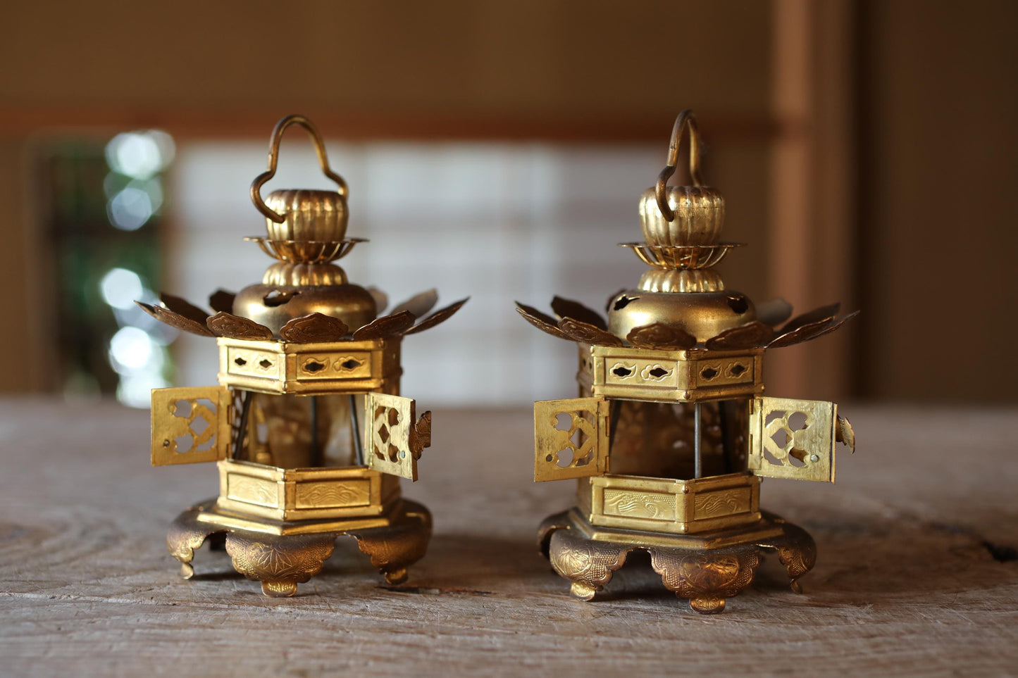 Two ornate golden lanterns with intricate designs are displayed on a wooden surface.