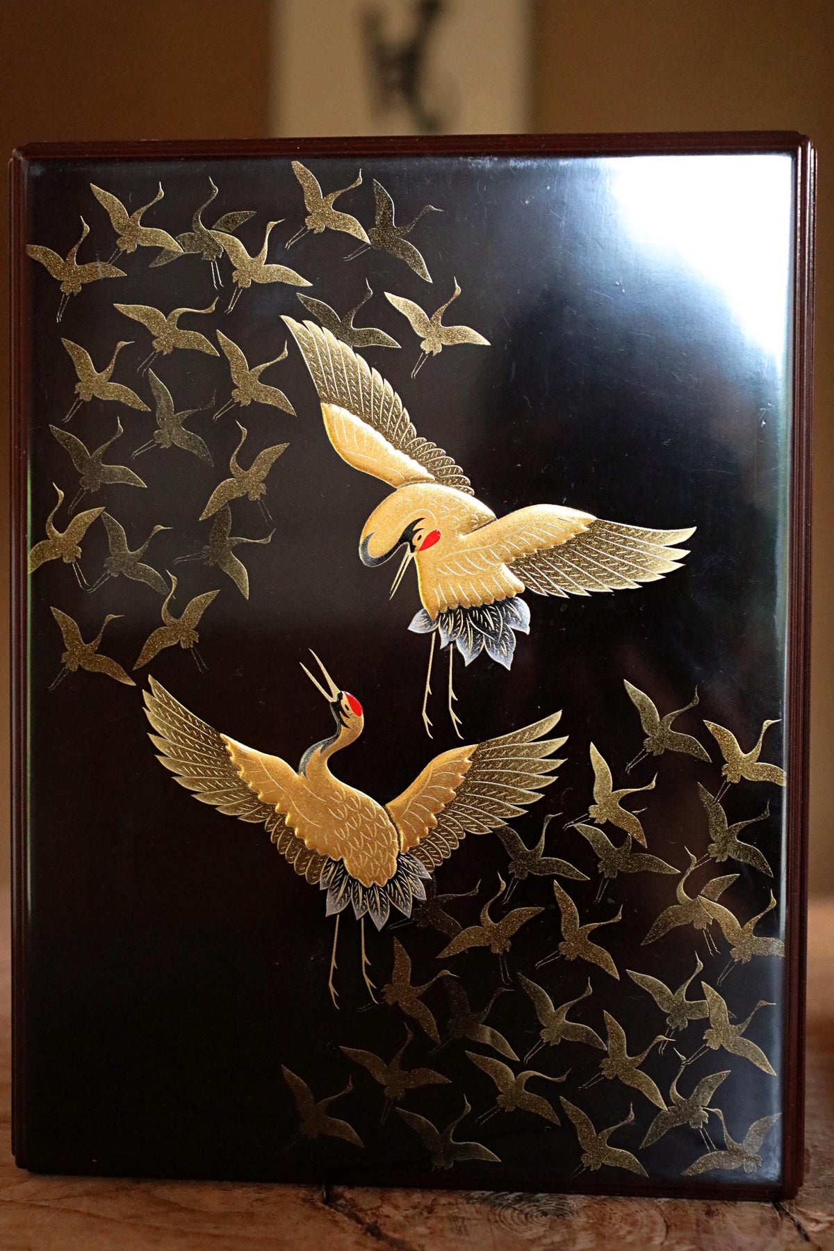 a black surface with a gold design depicting two cranes in flight, surrounded by a flock of cranes.