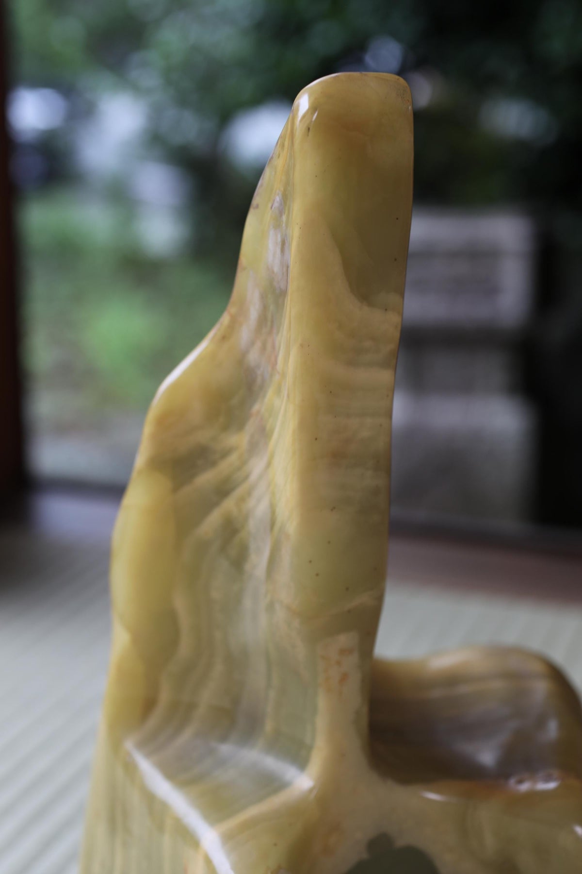 a close-up view of a yellowish-green, textured object, possibly a piece of art or a natural formation, with a blurred background that appears to be a garden or outdoor setting.