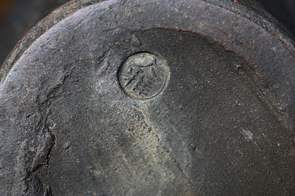 A close-up image of a dark, textured surface with a circular symbol or emblem in the center.