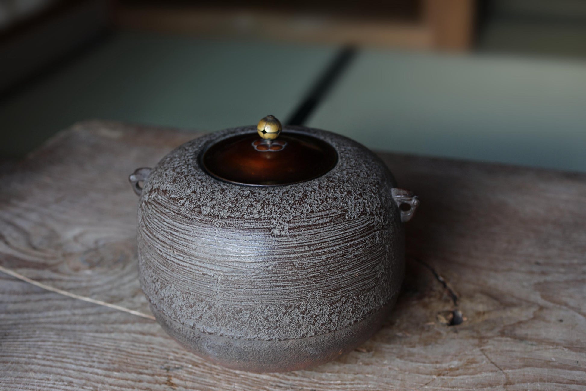A ceramic teapot with a dark brown lid sits on a wooden surface, with a blurred background.