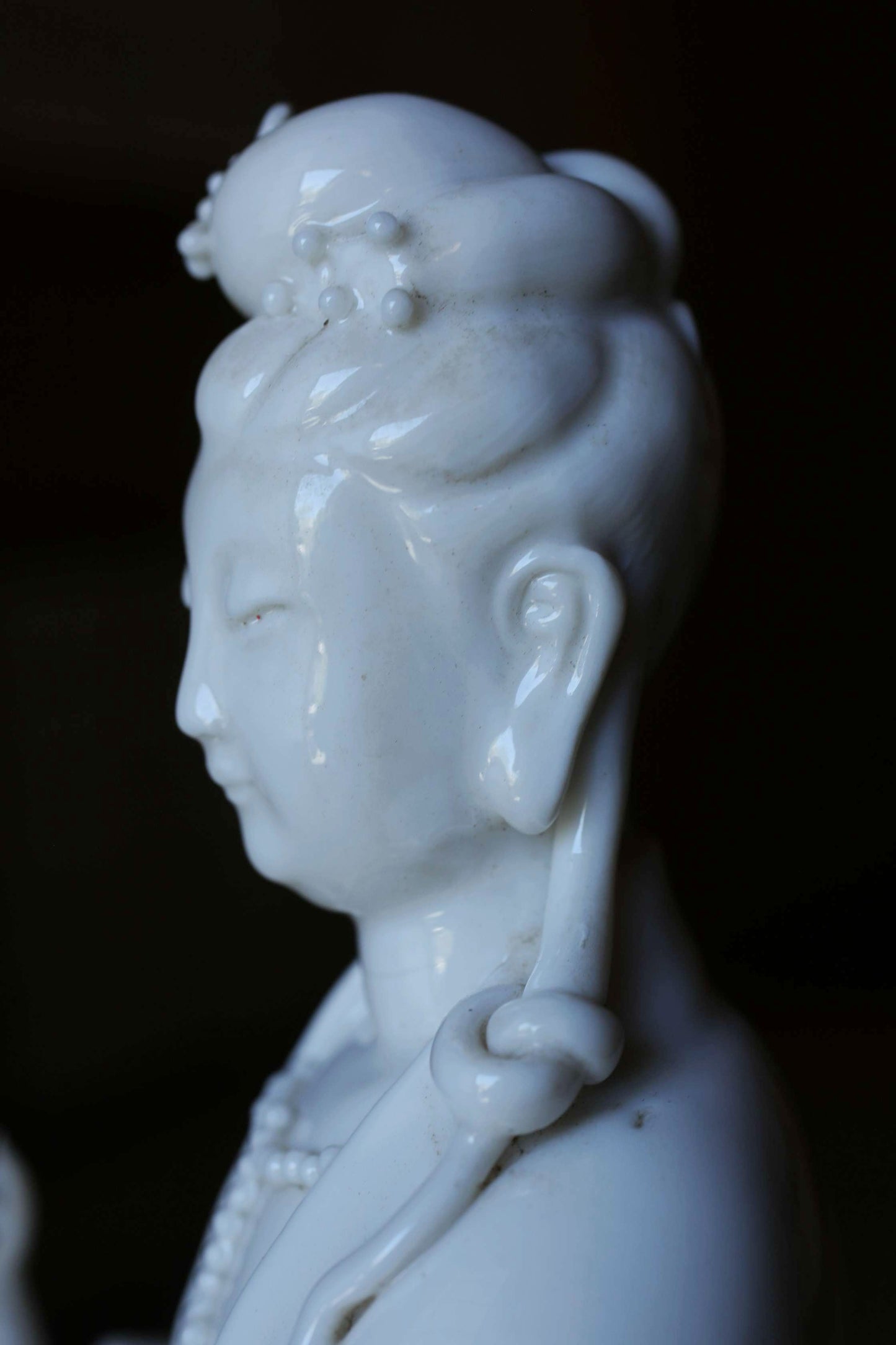 A close-up view of a white porcelain statue depicting a female figure with an ornate headdress and necklace.