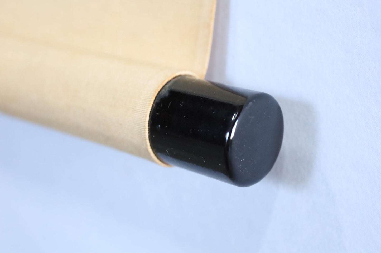 A close-up view of a black cap or lid attached to a beige or brown fabric, with a blue background.