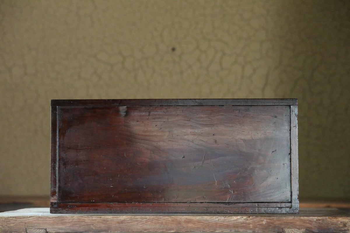 A dark wooden box sits on a wooden surface against a textured green background.