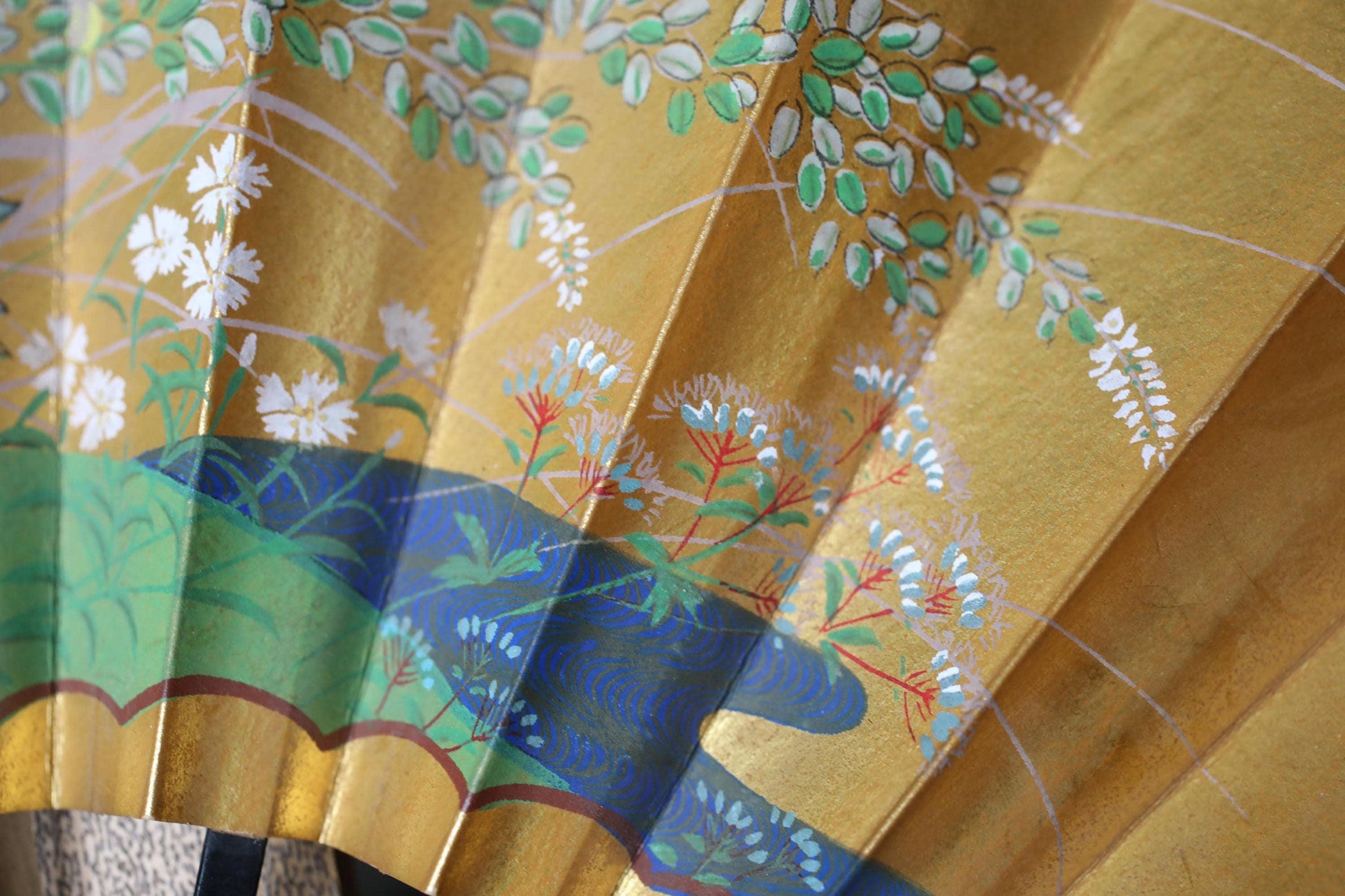 The image is a close-up of a decorative gold and blue fan with intricate floral patterns.