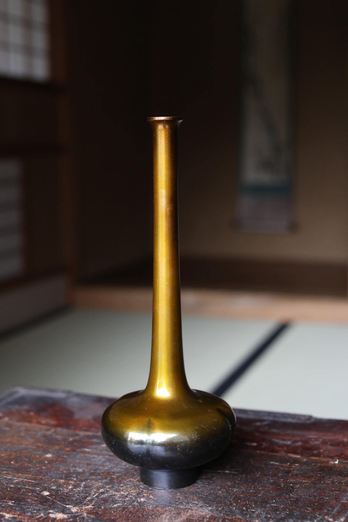 A golden vase with a narrow neck and wider base sits on a wooden surface.