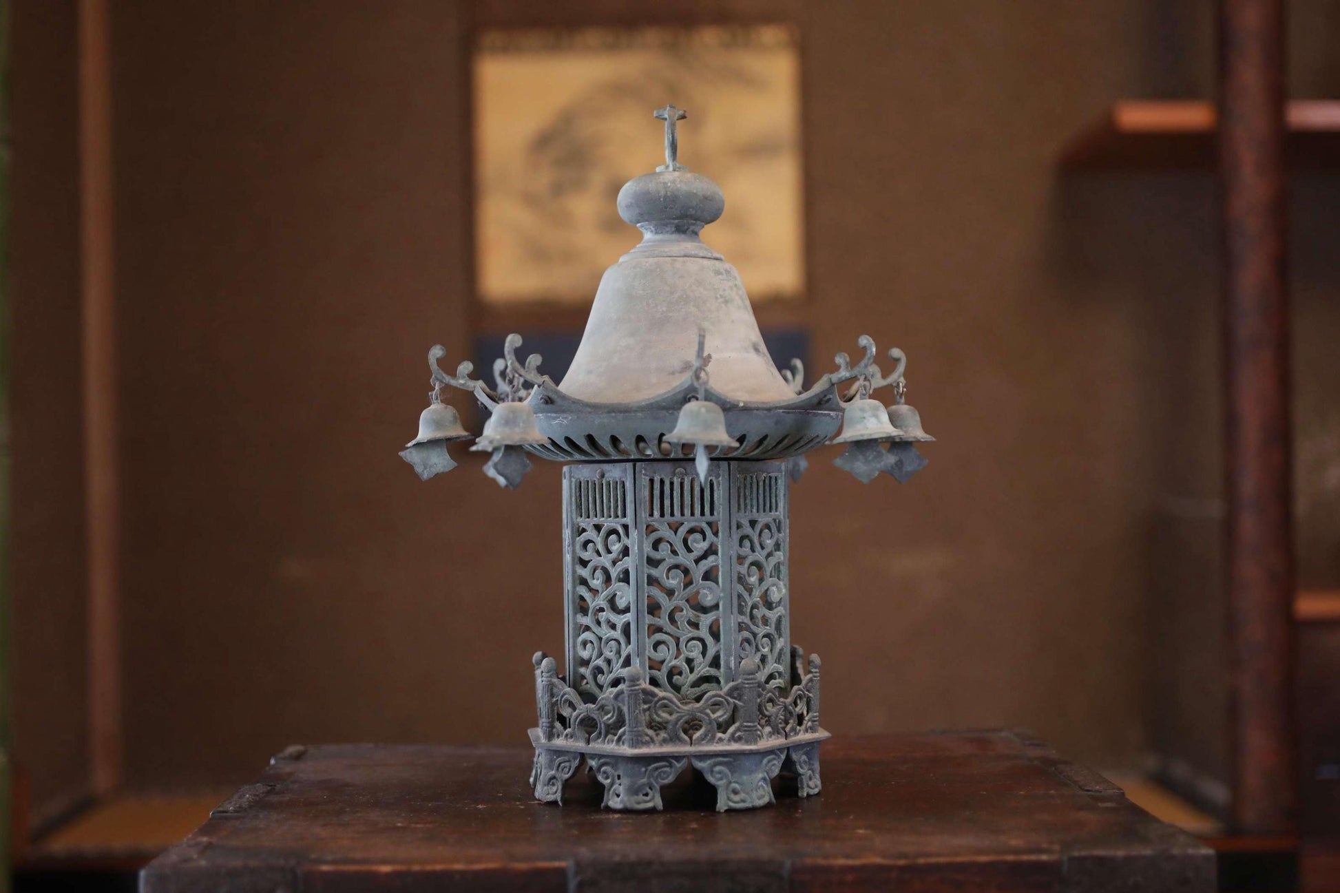 A decorative metal lantern with a pointed top and intricate designs, placed on a wooden surface against a brown background.