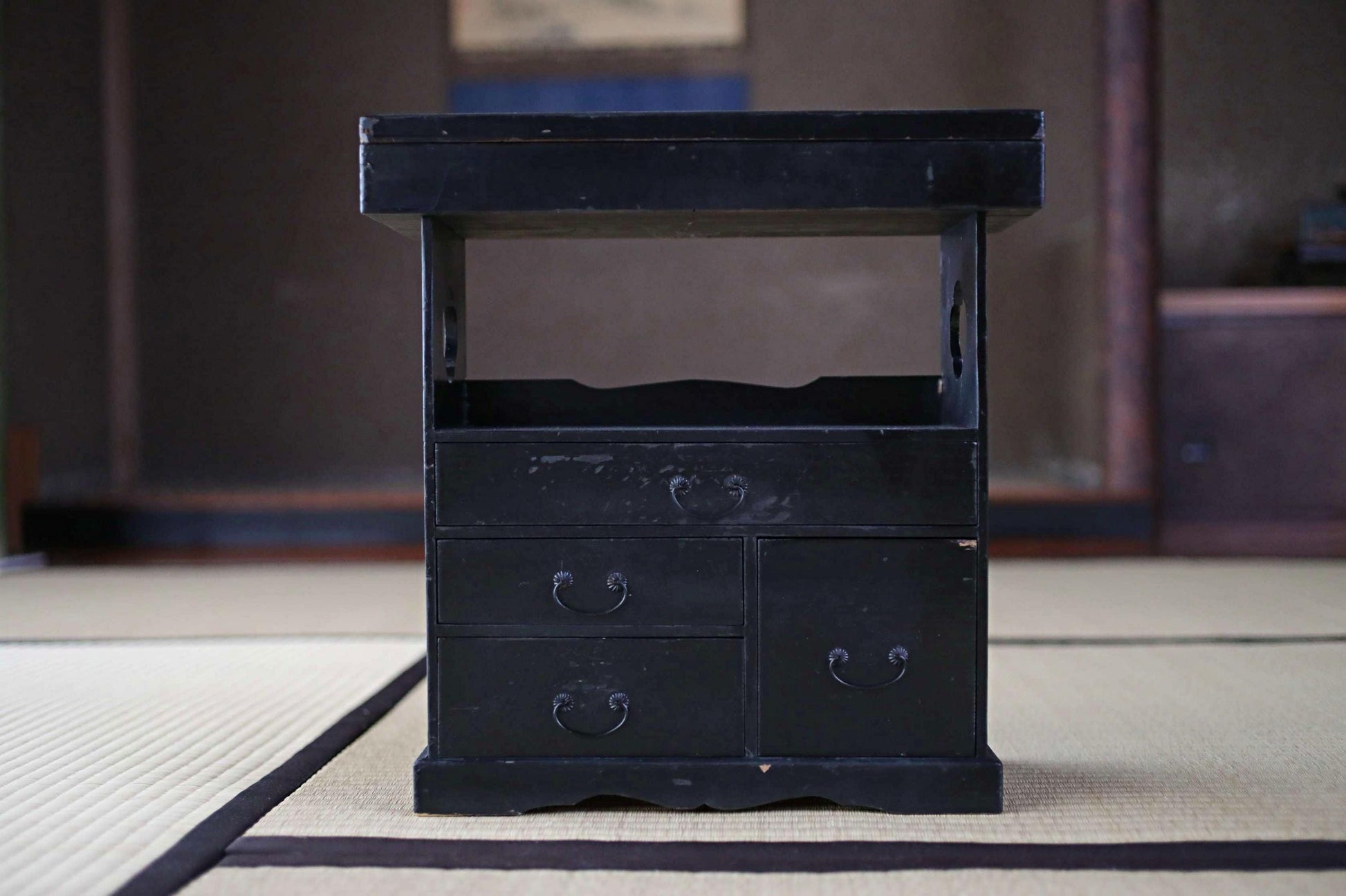 A black wooden cabinet with three drawers and a shelf, placed on a beige mat.