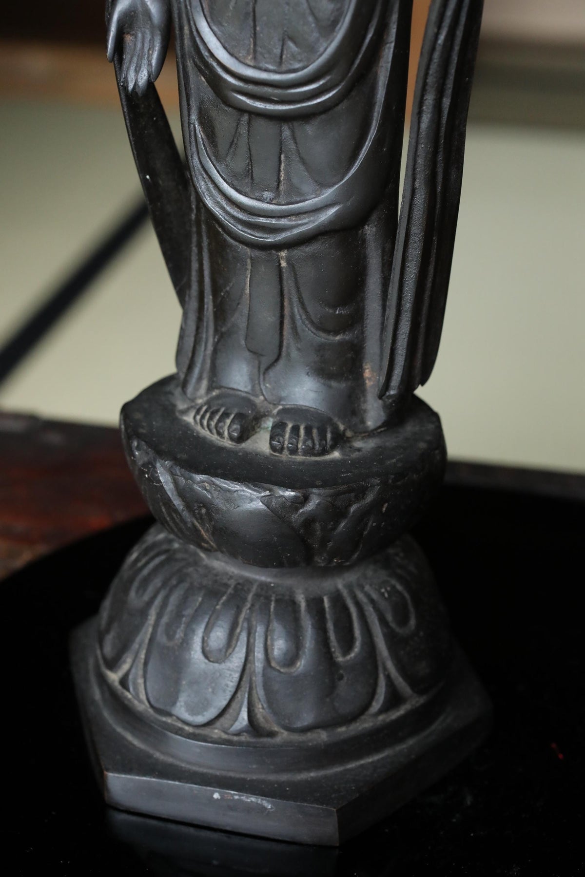 A close-up view of a dark-colored metal statue, possibly a religious figure, standing on a raised platform with intricate designs.