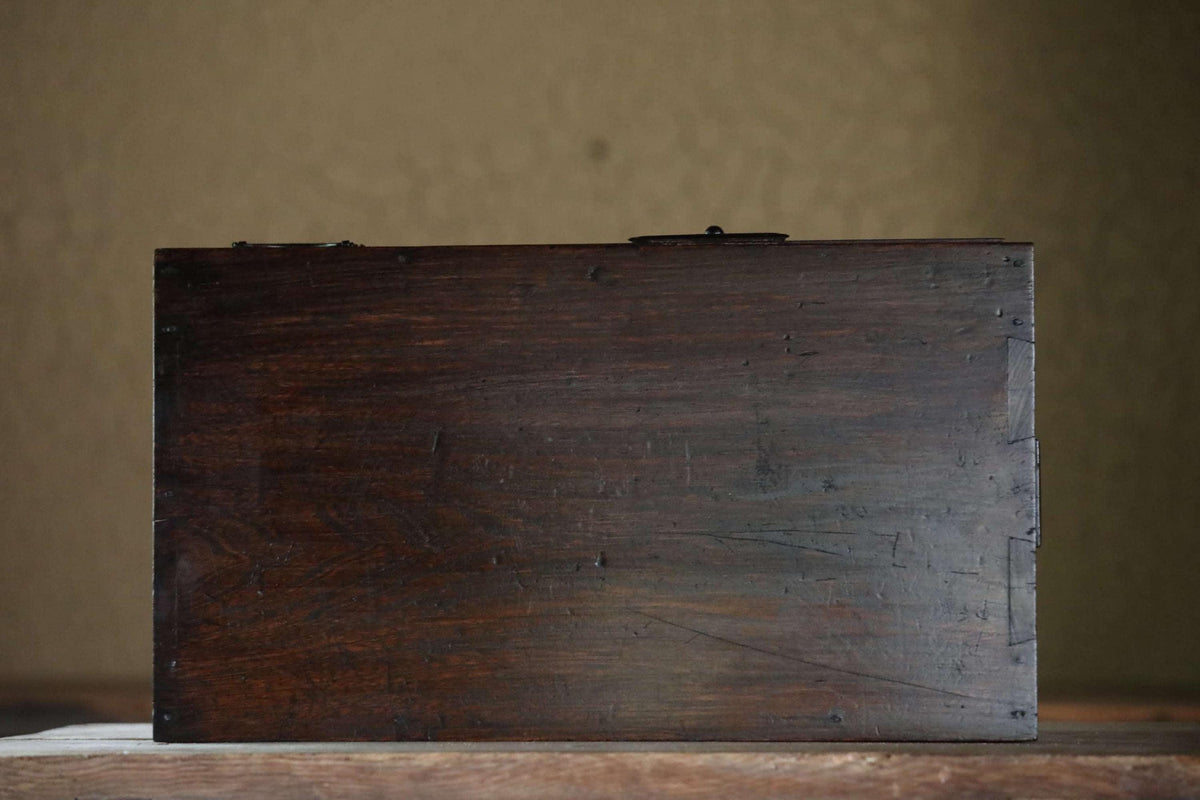 A dark wooden box sits on a wooden surface against a plain background.