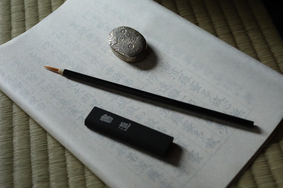 a black ink pen, a silver coin, and a piece of paper with Japanese characters on it, all resting on a woven mat.