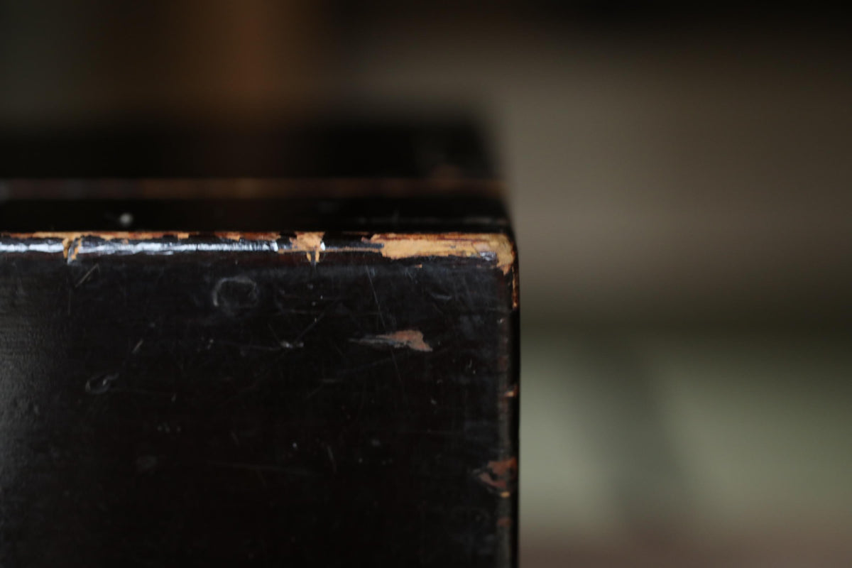 A close-up view of a dark wooden surface with visible scratches and marks, suggesting it has been used or exposed to the elements over time.