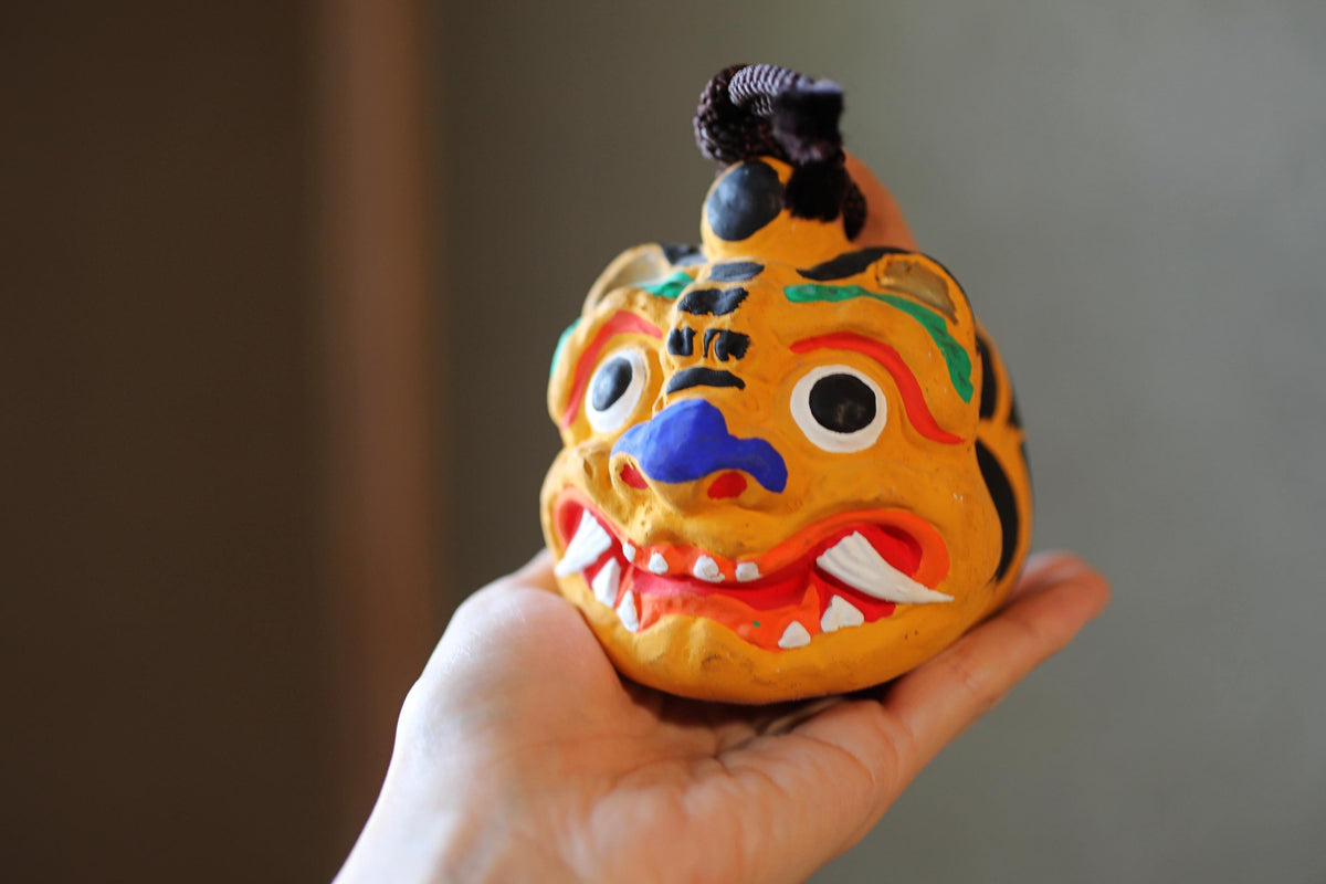 A hand holding a colorful, painted figurine of a tiger-like creature with a black and white striped pattern.