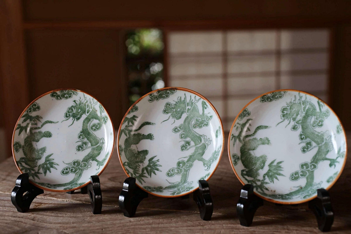 Three ornate plates with green dragon designs are displayed on a wooden surface.