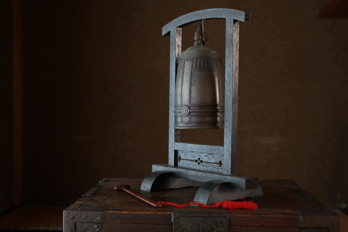 A metal bell with a red tassel is displayed on a wooden stand against a dark background.