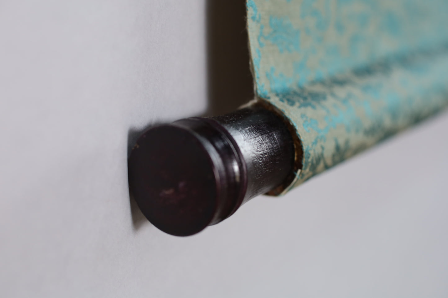 A close-up view of a dark-colored metal object, possibly a drawer handle or a drawer pull, attached to a wall.